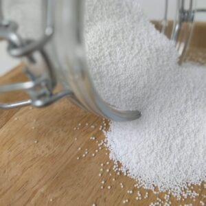 Bocal en verre renversé laissant s’échapper des granulés blancs. Agent blanchissant naturel pour linge et surfaces | commercialisé par la boutique Tipi à Theux
